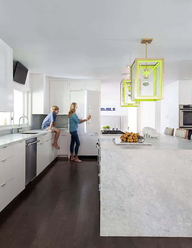Modern kitchen with two islands featuring sleek cabinetry, marble countertops, and vibrant pendant lights. Bright, airy space with dark hardwood flooring.