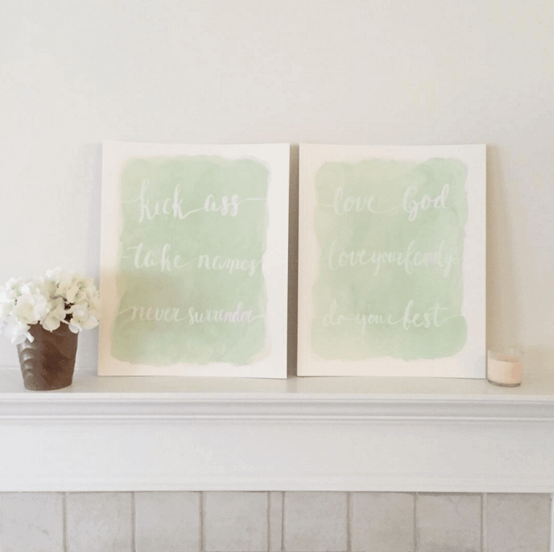 Two framed prints with soft green backgrounds featuring motivational texts in white cursive, placed on a light mantel with a vase of white flowers.