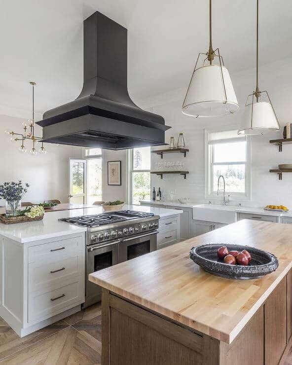 Spacious modern farmhouse kitchen with two large islands featuring butcher block countertops, white cabinetry, and herringbone flooring.