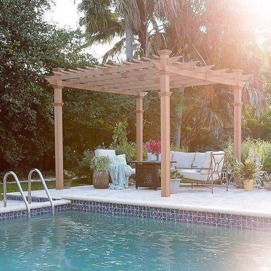 25 Pool Pergola Ideas for a Relaxing Oasis 7 Wooden pergola with a lattice top over a serene pool area, providing shade and a modern outdoor lounging space surrounded by tropical greenery.