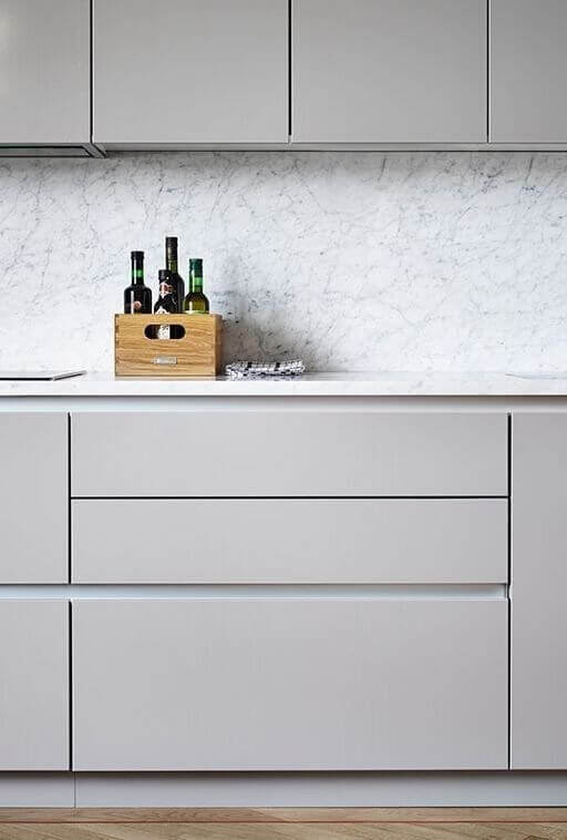 Modern kitchen cabinetry with sleek gray finishes, soft-close drawers, and white marble backsplash. Features wooden crate for storage warmth.