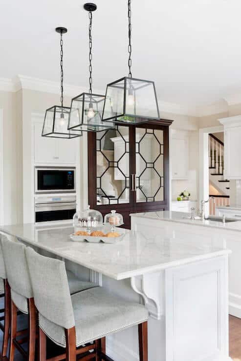 Contemporary kitchen with two central islands featuring white marble countertops, flanked by upholstered stools and modern pendant lights.