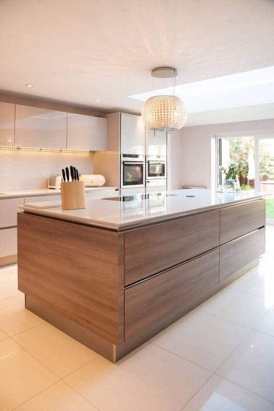 Expansive kitchen island with a sleek wooden base and white countertop, surrounded by high-gloss cabinets and natural light.