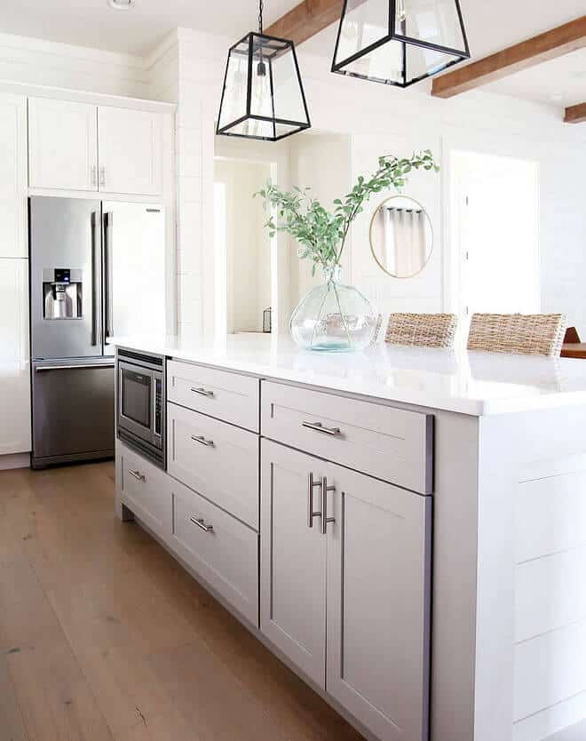 Spacious kitchen island with white quartz countertop for prep and dining. Soft gray cabinetry, light wood flooring, and modern black pendant lights.