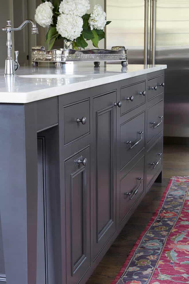 Deep charcoal gray kitchen island with a white quartz countertop, ample storage, floral decor, and vibrant area rug, enhancing modern kitchen layout.