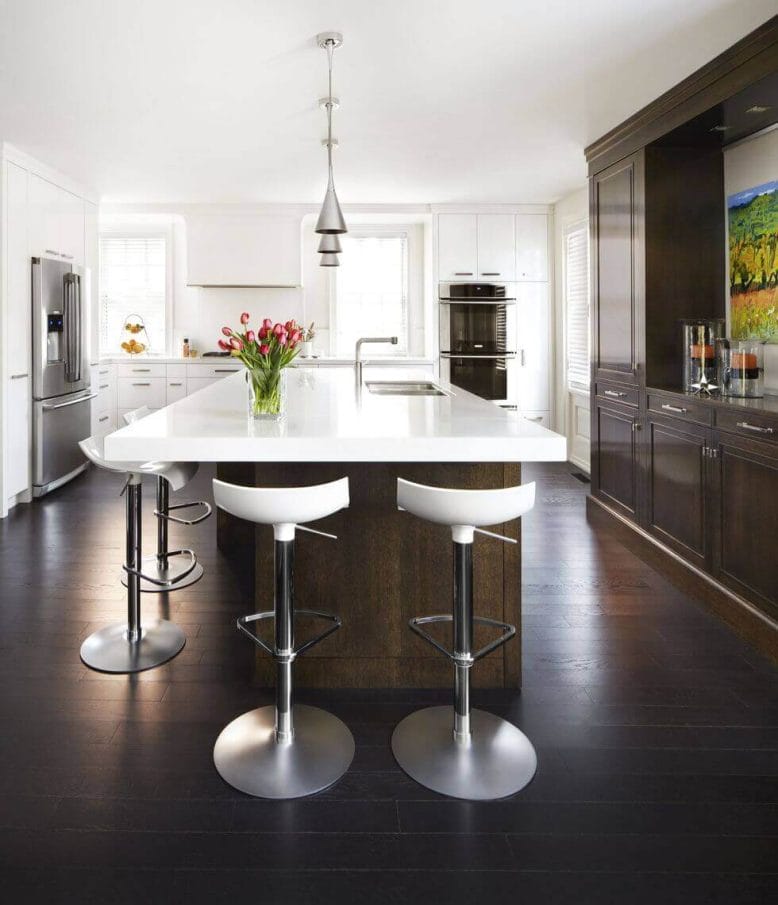 Central kitchen island with white quartz countertop, dark wood cabinetry, stainless steel appliances, and modern bar stools in a sunlit space.