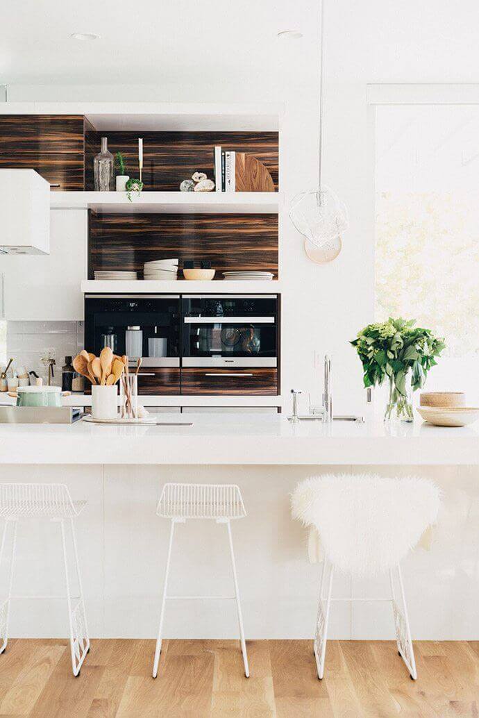 Modern kitchen with white quartz countertops, natural wood shelving, and sleek metal bar stools, creating a bright, open space.