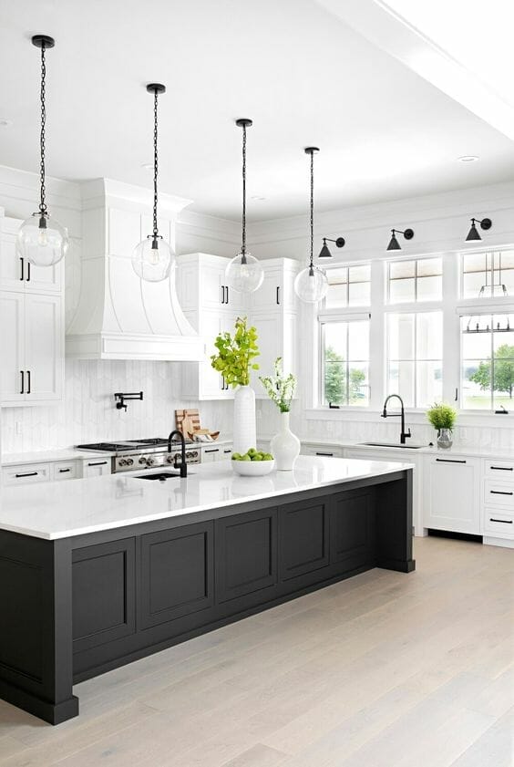 Modern farmhouse kitchen with a large black island and white marble countertop. White cabinetry, natural light, and warm hardwood floors create an airy, functional space.