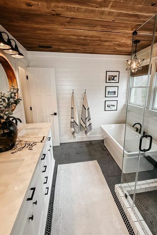Bright bathroom with white shiplap walls and natural wood ceiling. Features a freestanding tub, glass shower, and double sink vanity.